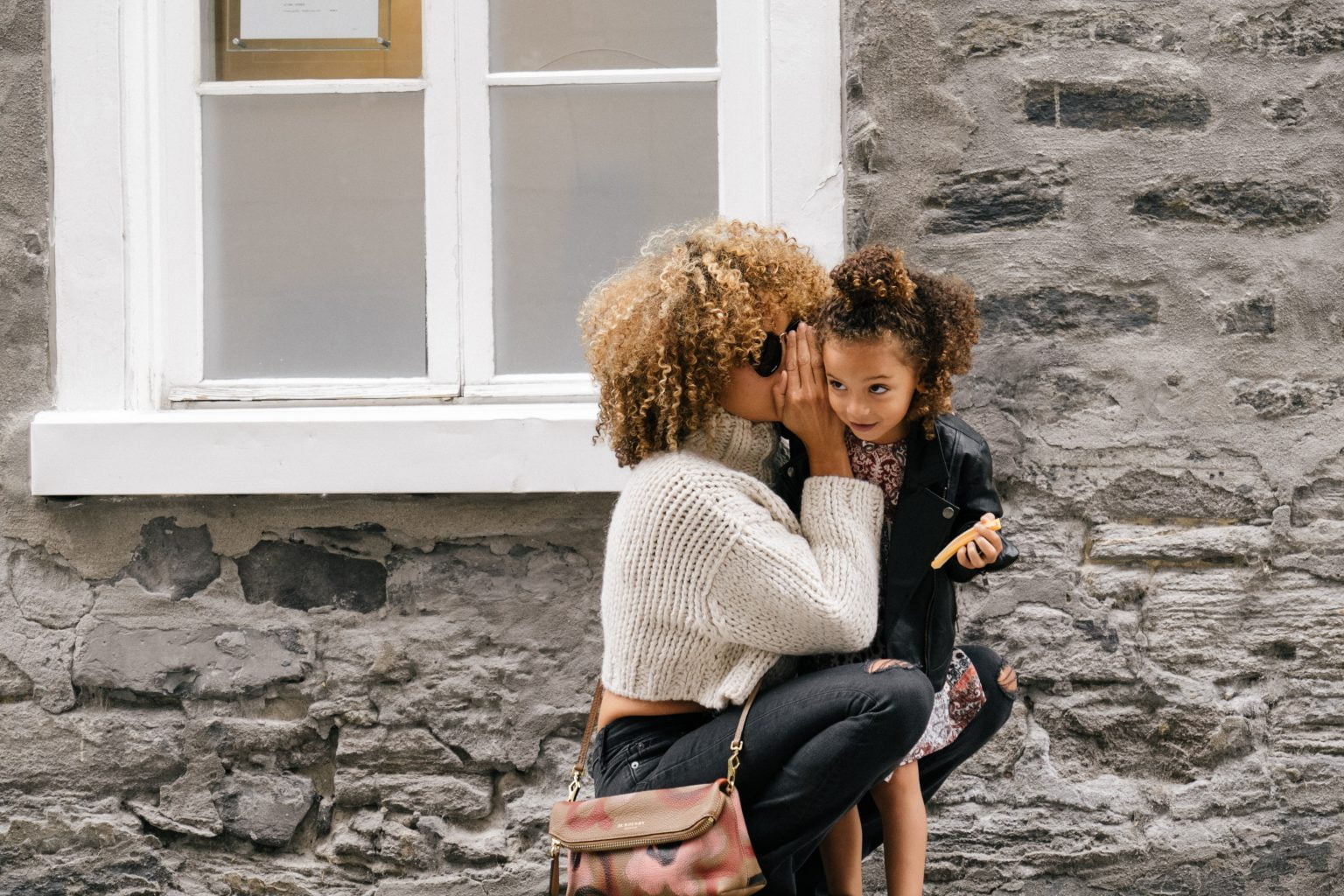 woman whispering in young girl's ear